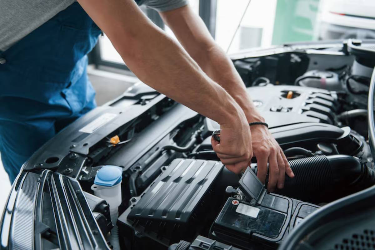 A mechanic working on a car engine, adjusting components and inspecting the battery under the hood of a vehicle.