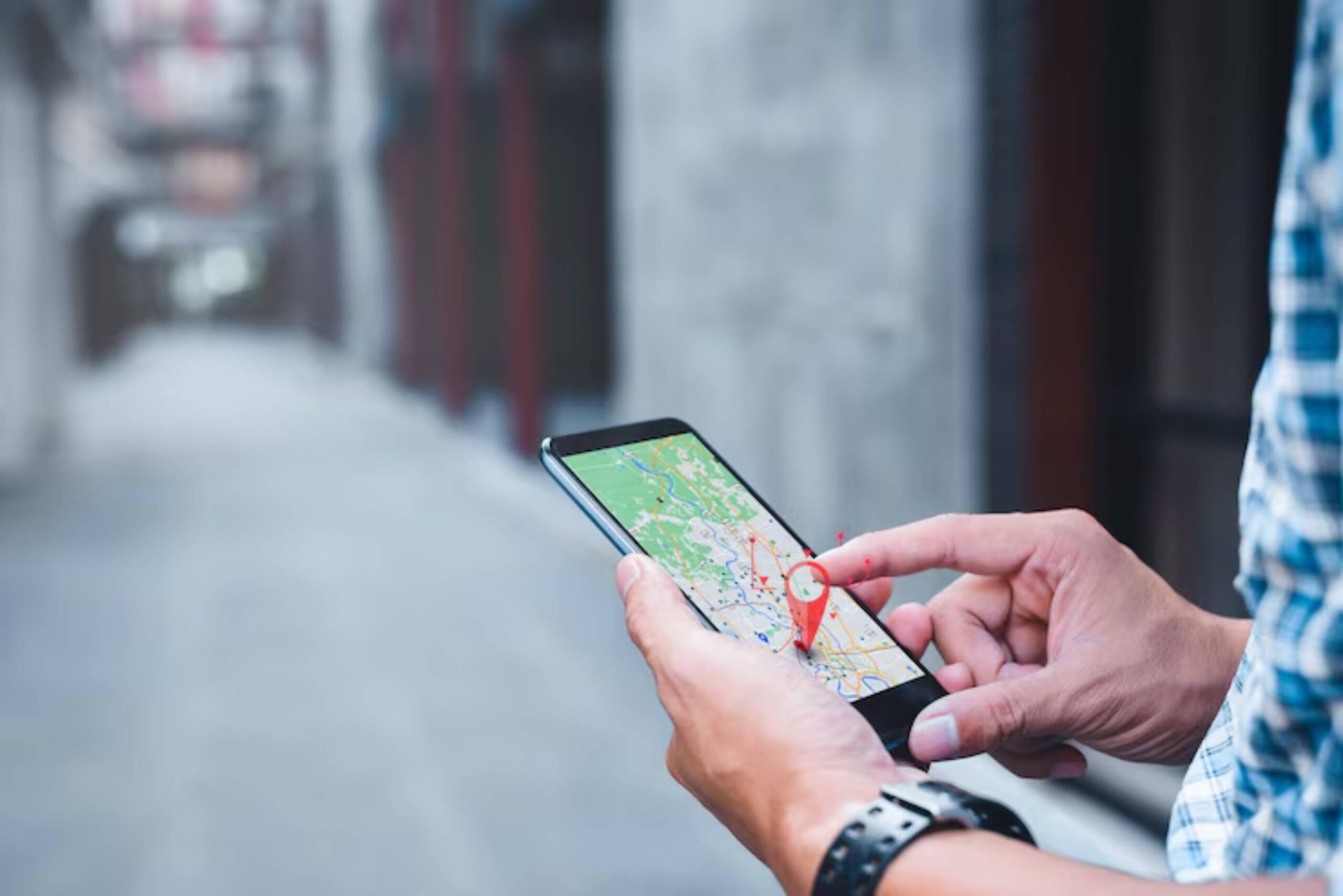 A person uses a smartphone to navigate with a map, featuring a red location pin, in a blurred alleyway.