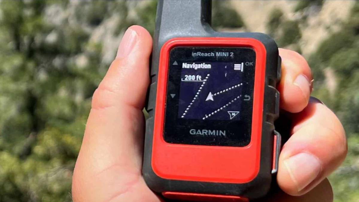 A person holds a Garmin inReach Mini 2 device, displaying navigation with a distance reading of 200 ft against a natural background.