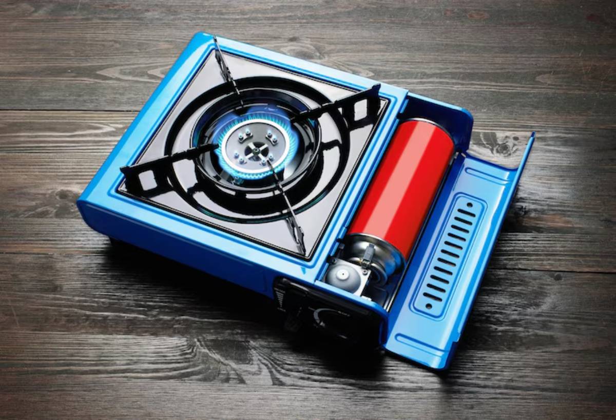 Portable blue gas stove with a round burner and red gas cylinder, placed on a dark wooden surface.