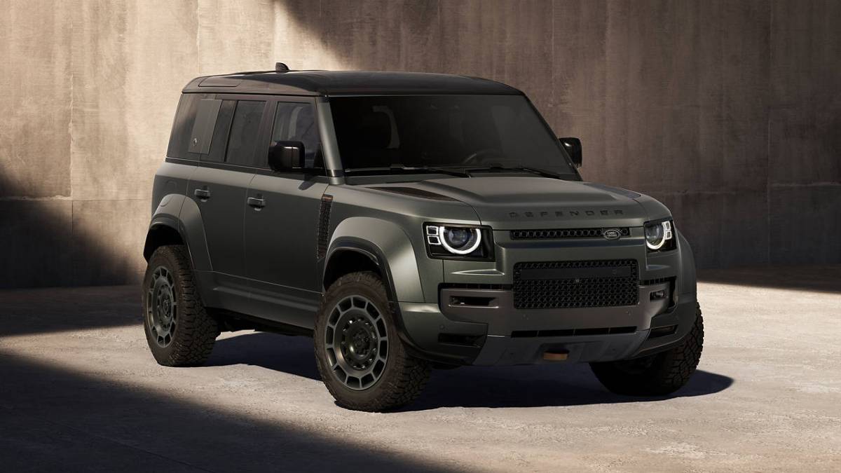 A rugged, dark green Land Rover Defender parked in a shadowy industrial setting, showcasing its bold design and off-road capabilities.
