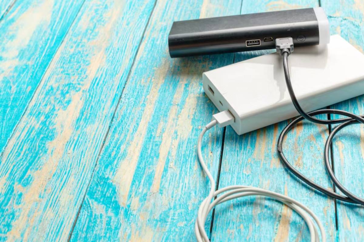 Two power banks, one black and one white, connected by charging cables, resting on a vibrant turquoise wooden surface.