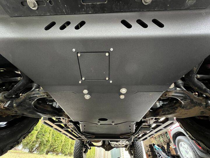 Underside view of a vehicle showcasing a sturdy black metal skid plate with ventilation slots and secure mounting bolts.