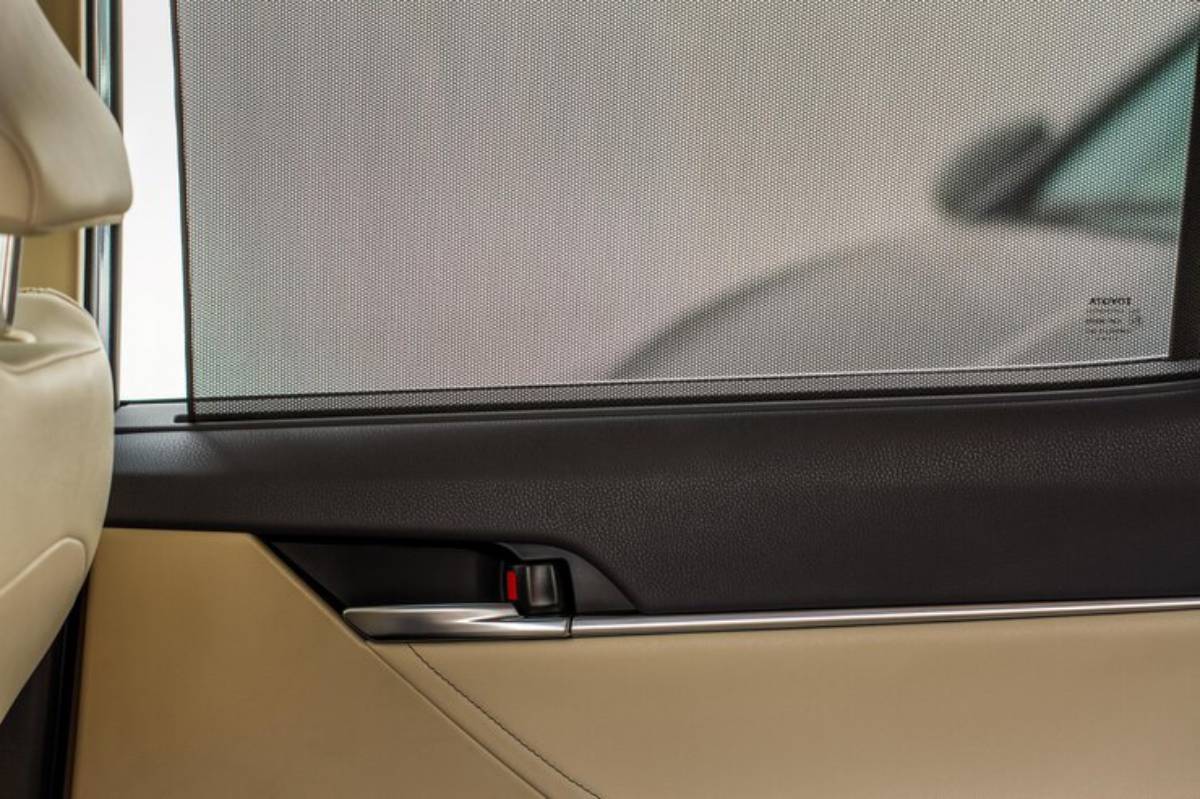 Interior view of a car's rear door featuring a mesh sunshade, leather upholstery, and a metallic door handle.
