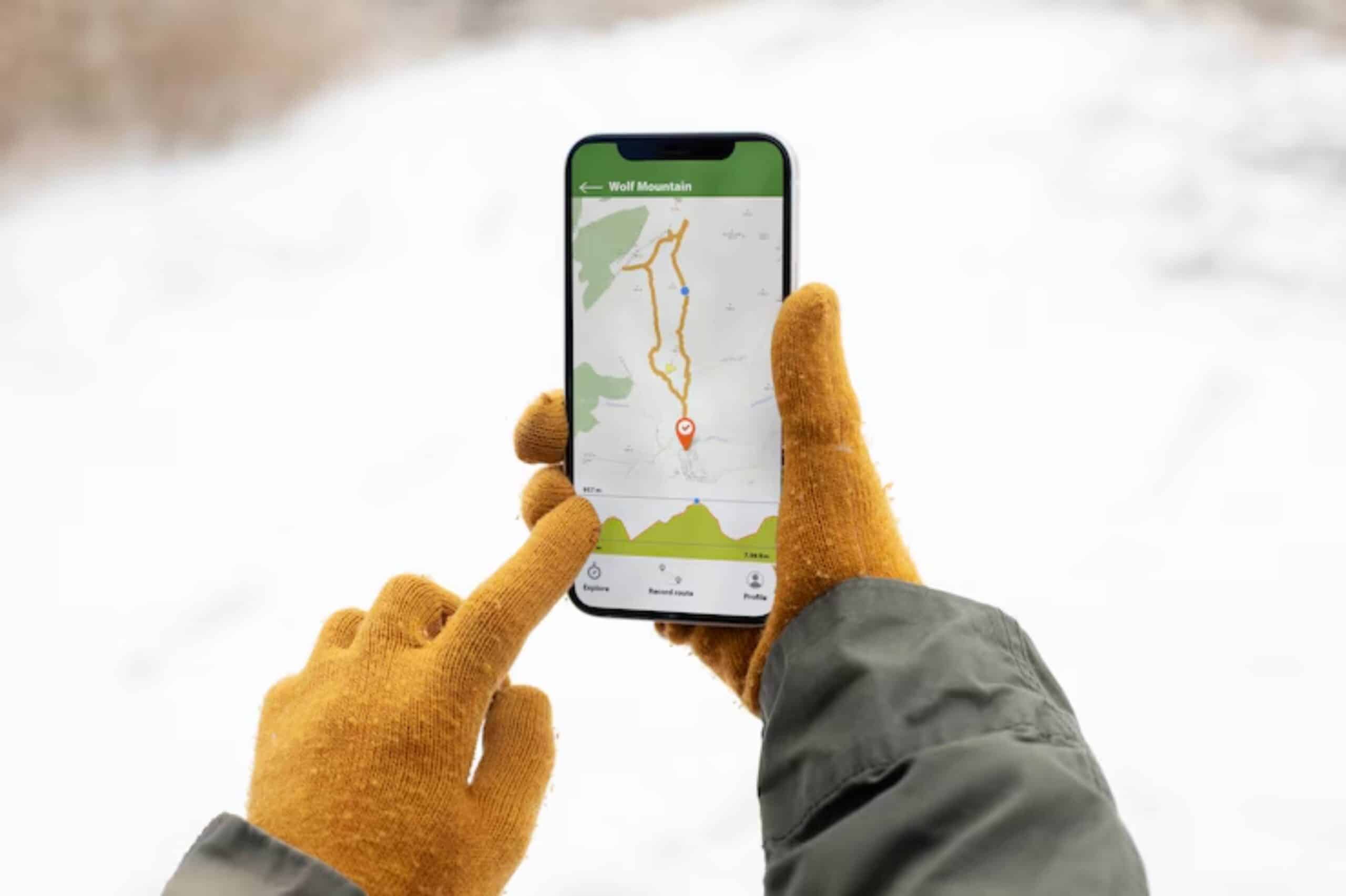 A person in a winter coat and orange gloves navigates a snow-covered area using a smartphone with a map of Wolf Mountain.