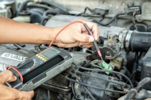 A mechanic testing electrical connections in a car engine with a multimeter, focusing on wires and components for diagnosis.
