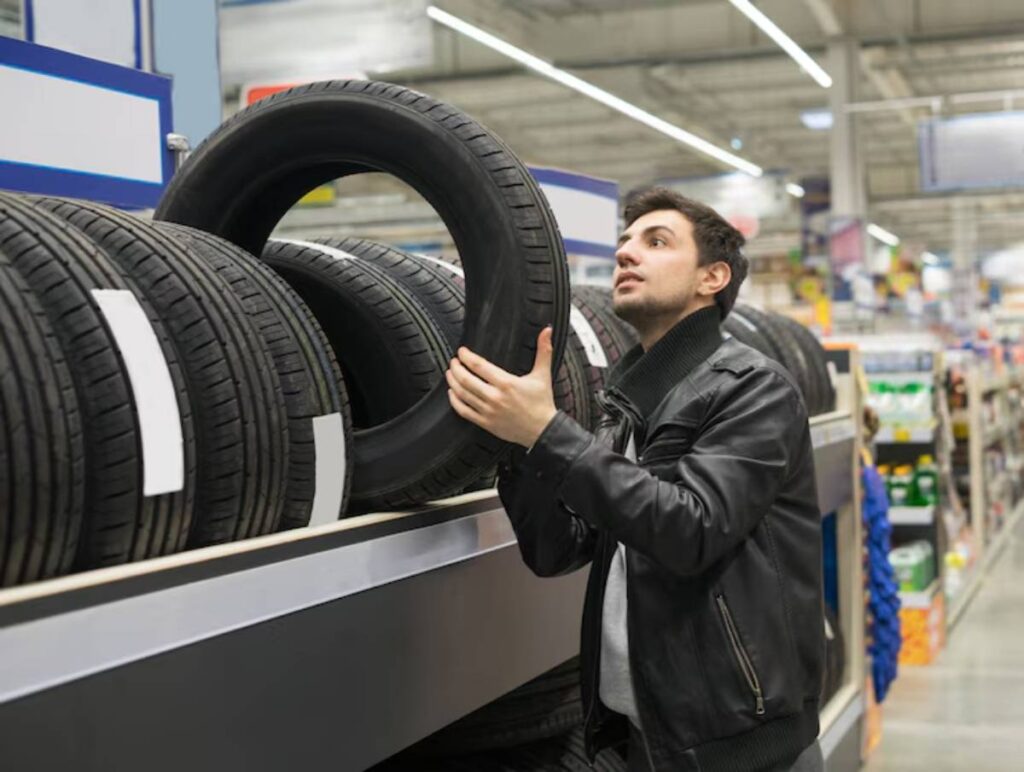 A person in a leather jacket examines a tire in a store, surrounded by neatly stacked tires on display.