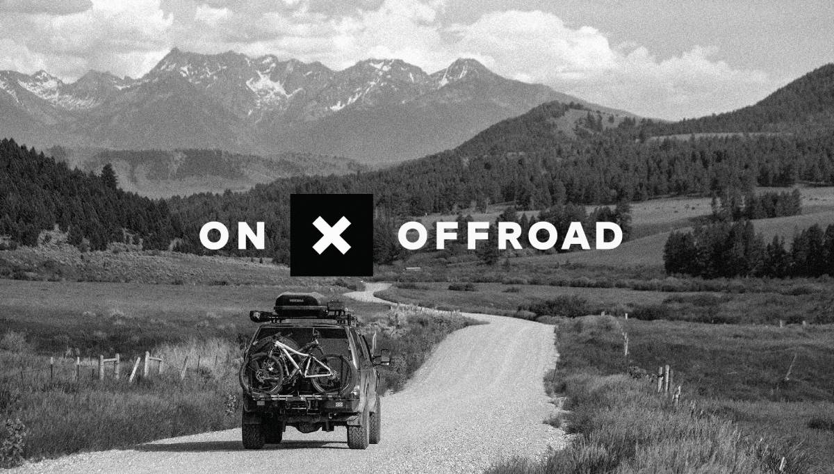 A vehicle with bikes on its roof travels down a gravel road, surrounded by mountains and trees, with ON X OFFROAD overlay.