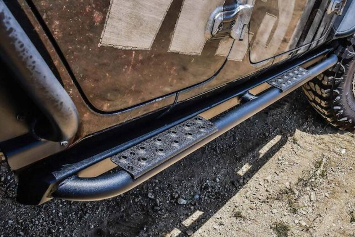 Close-up of a black metal side step on an off-road vehicle, mounted above gravel, showcasing textured grip and rugged design.